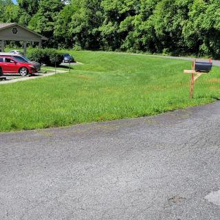 A serene residential scene featuring a mailbox along a curved driveway with parked cars and lush green grass.