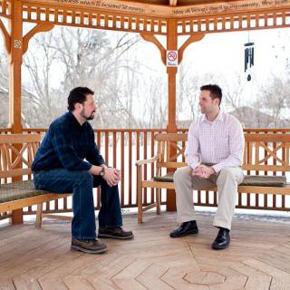 Two people having a conversation in a wooden gazebo.