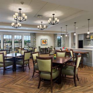 A beautifully designed dining area featuring elegant chandeliers, wooden tables with cushioned chairs, and a spacious layout with a view of the kitchen.