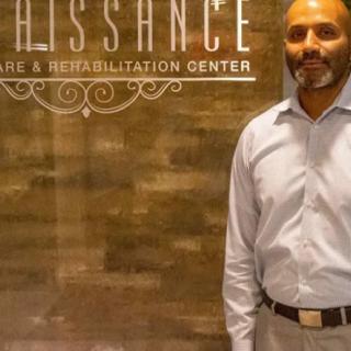 A man stands in front of a sign at a rehabilitation center.