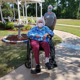 An elderly individual in a wheelchair enjoys the outdoors with a caregiver.