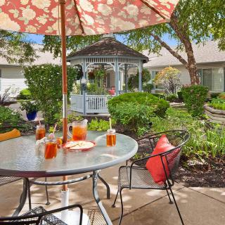 A cozy patio setup with a table, umbrella, and chairs overlooking a lush garden and gazebo.