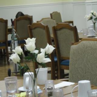 A dining area with tables adorned with white roses in vases, surrounded by upholstered chairs.