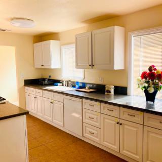 A bright and modern kitchen with white cabinets, a dark countertop, and a vase of flowers by the window.