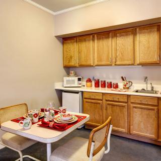 A cozy kitchen with a dining area, featuring wooden cabinets, a microwave, and a table set with red-accented tableware.