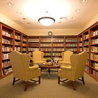 A cozy library with armchairs surrounded by bookshelves filled with books.