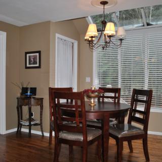 A cozy dining room with a round wooden table, chairs, and a chandelier by the window.
