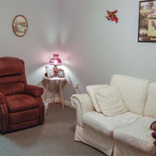 A cozy living room featuring a white sofa, a red armchair, a side table with a lamp, and various wall decorations.