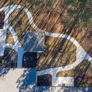 Aerial view of a modern landscape design featuring curved concrete paths and long shadows.
