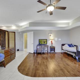 Spacious bedroom with wood flooring, featuring a ceiling fan, dresser, television, and a desk.