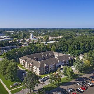 Aerial view of an apartment complex surrounded by trees and a parking lot in a suburban area.