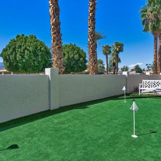 A well-maintained outdoor putting green surrounded by palm trees and a white fence.
