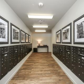 A well-lit mailroom hallway with rows of mailboxes and framed photos on the walls.