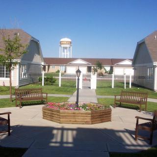 A peaceful courtyard with benches and a pathway leading to nearby buildings, with a water tower visible in the background.