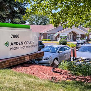 A sign for Arden Courts with a building and parked cars in the background.