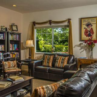 A cozy living room with leather sofas, a bookshelf, and a large window letting in natural light.