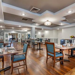 A modern dining room with neatly arranged tables and chairs, featuring wooden floors and elegant lighting.