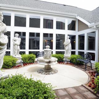 A serene courtyard featuring a central fountain surrounded by statues and lush greenery.