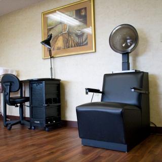 A salon interior featuring a hair dryer chair and a workspace desk beside a painting.