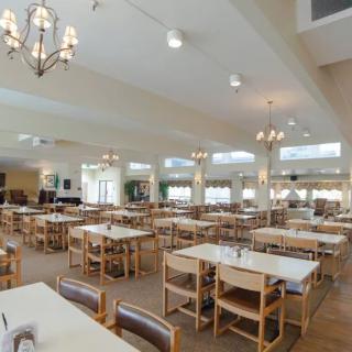 An empty dining hall with neatly arranged tables and chairs, illuminated by chandeliers.