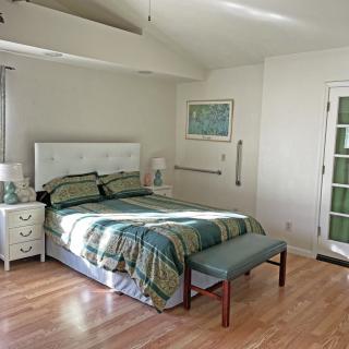 A cozy bedroom with a neatly made bed, nightstand, and lamp on a hardwood floor.