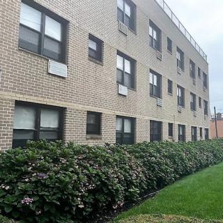 A brick apartment building surrounded by green bushes and a well-kept lawn.