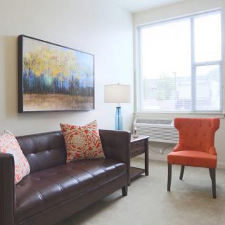 A cozy living room with a brown sofa, orange chair, and a colorful painting on the wall.