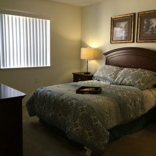 A cozy bedroom with a neatly made bed, a bedside lamp, and framed artwork on the walls.