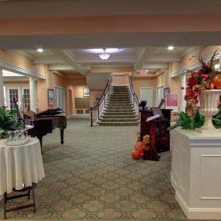 A spacious lobby area featuring a grand piano, decorative plants, and an elegant staircase.