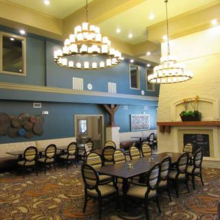 A spacious dining room featuring elegant chandeliers, a long table with chairs, and a cozy fireplace.