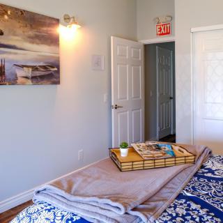 A cozy bedroom with a neatly arranged bed featuring a decorative tray, artwork on the wall, and an open door leading to another room.