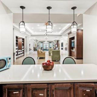 A modern kitchen with white countertops and wood cabinetry, featuring pendant lighting and an open layout.