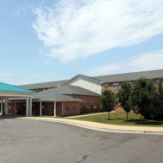 A modern healthcare facility viewed from the entrance, featuring a blue awning and landscaped surroundings.