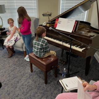 Children participating in a music lesson by the piano.