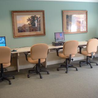 A computer lab with workstations and chairs lined against the wall, featuring framed paintings above.
