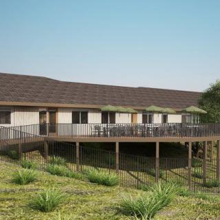 A modern building with a wooden deck overlooking a landscaped area with greenery.