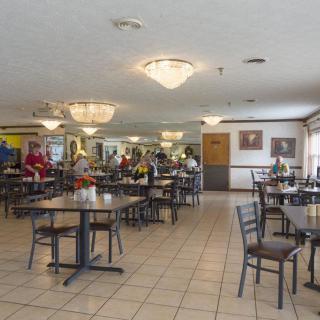 A spacious cafe with empty tables and a few people gathered around a counter.