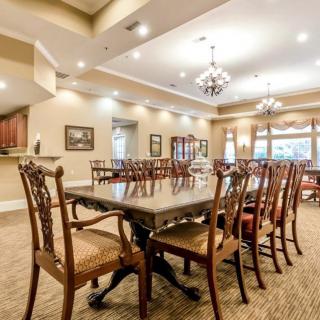 Elegant dining room with a large table and ornate chairs, illuminated by chandeliers.