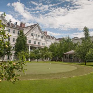 A grand hotel surrounded by lush greenery and a well-maintained lawn under a partly cloudy sky.