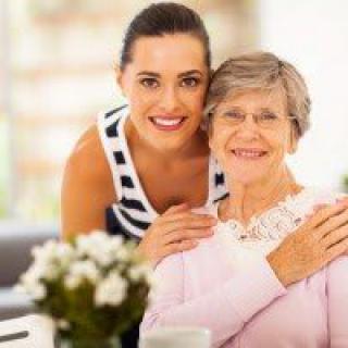 A young woman and an elderly woman smiling together indoors.