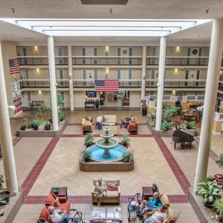 A spacious hotel atrium featuring a central fountain, seating areas, and lush greenery under ample natural lighting.