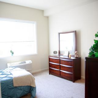 A bright and minimalist bedroom with a bed, dresser, and mirror.