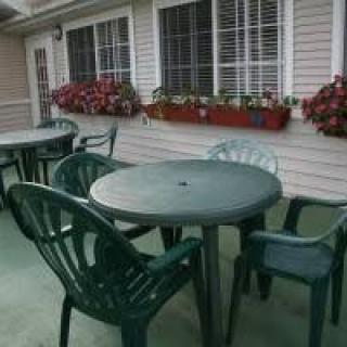 An outdoor patio area with green plastic chairs and tables, adorned with flower boxes on the windowsills.