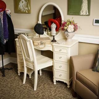 A vintage vanity set with a mirror and chair, adorned with hats and a floral arrangement.