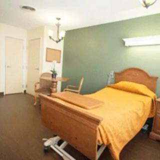 A neatly arranged hospital room featuring a single bed with orange bedding, wooden furniture, and a calm atmosphere.