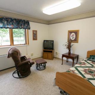 A cozy bedroom with a wooden bed, a TV on a stand, a comfortable chair, and decorative elements.