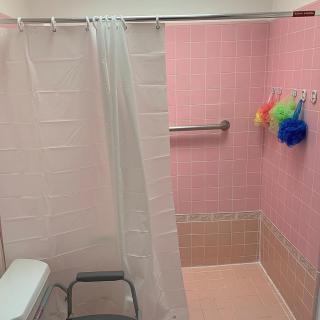 A bathroom with pink tiles, a shower curtain, and colorful loofahs hanging from a towel rack.