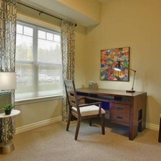 A cozy home office with a desk by the window, featuring a lamp and artwork on the wall.