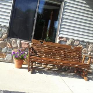 A wicker bench on a patio next to a planter with flowers, set against a stone wall.