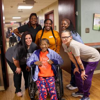 A joyful moment captured with a group of healthcare workers and an elderly woman in a wheelchair, showcasing community and support.
